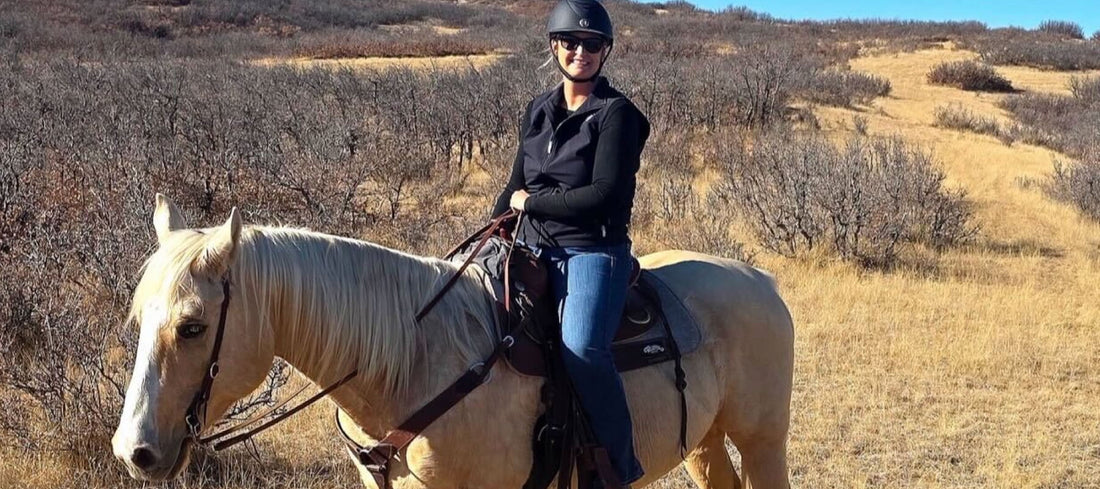Trish smiling at the camera while sitting on her horse with mountains in the background 