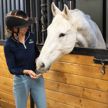 Dr. Chelsea Luedke with a calm white horse in a barn