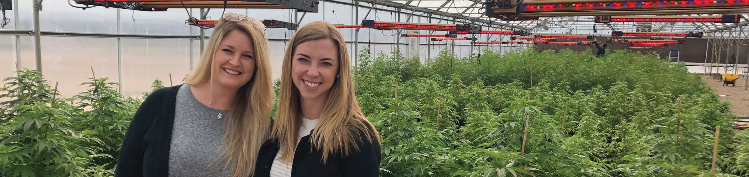 Chelsea and Trish, founders of VetCS standing in a greenhouse with plants around them.