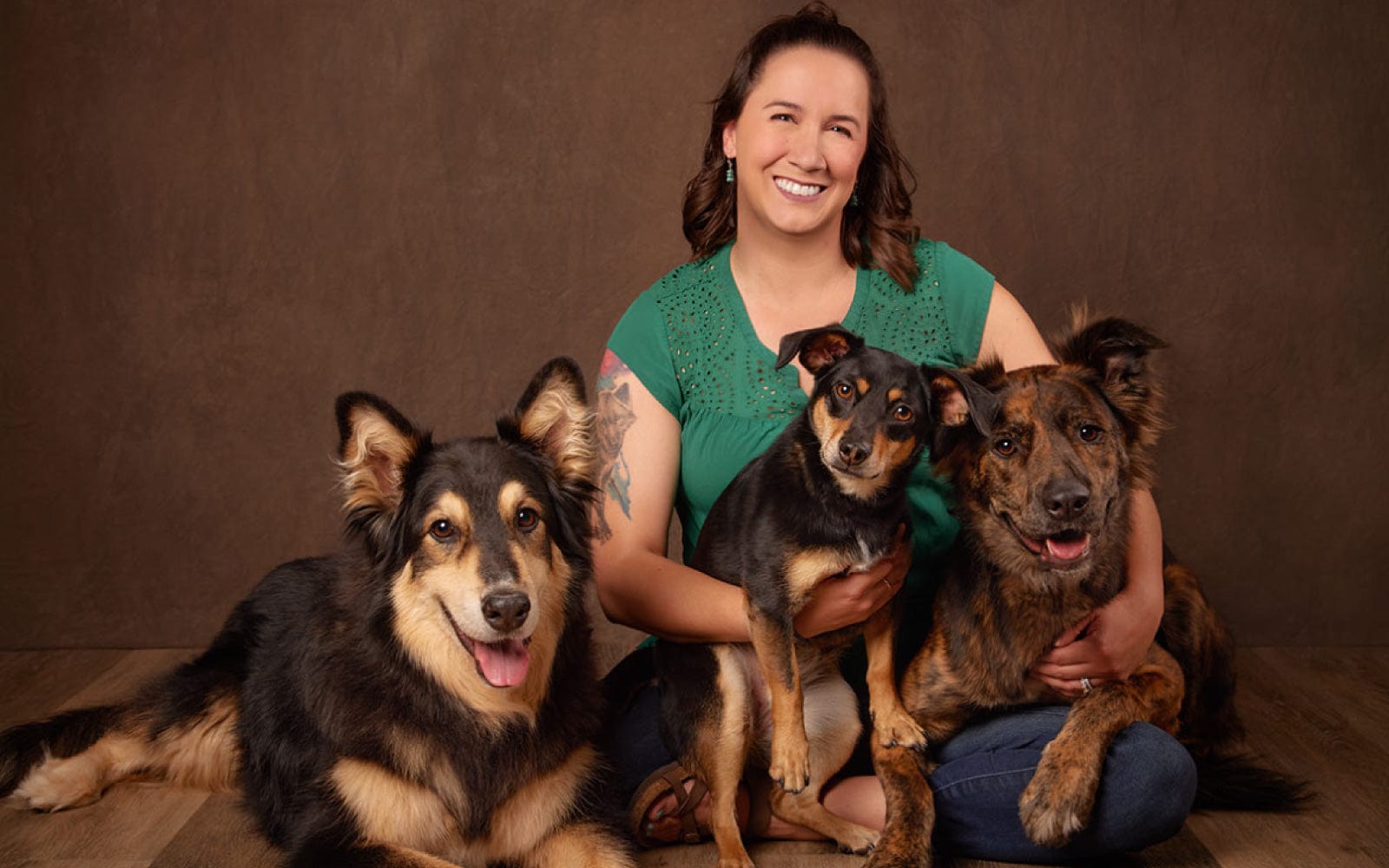 Veterinary professional Emily sitting on the floor with three happy dogs, smiling in front of a studio backdrop.